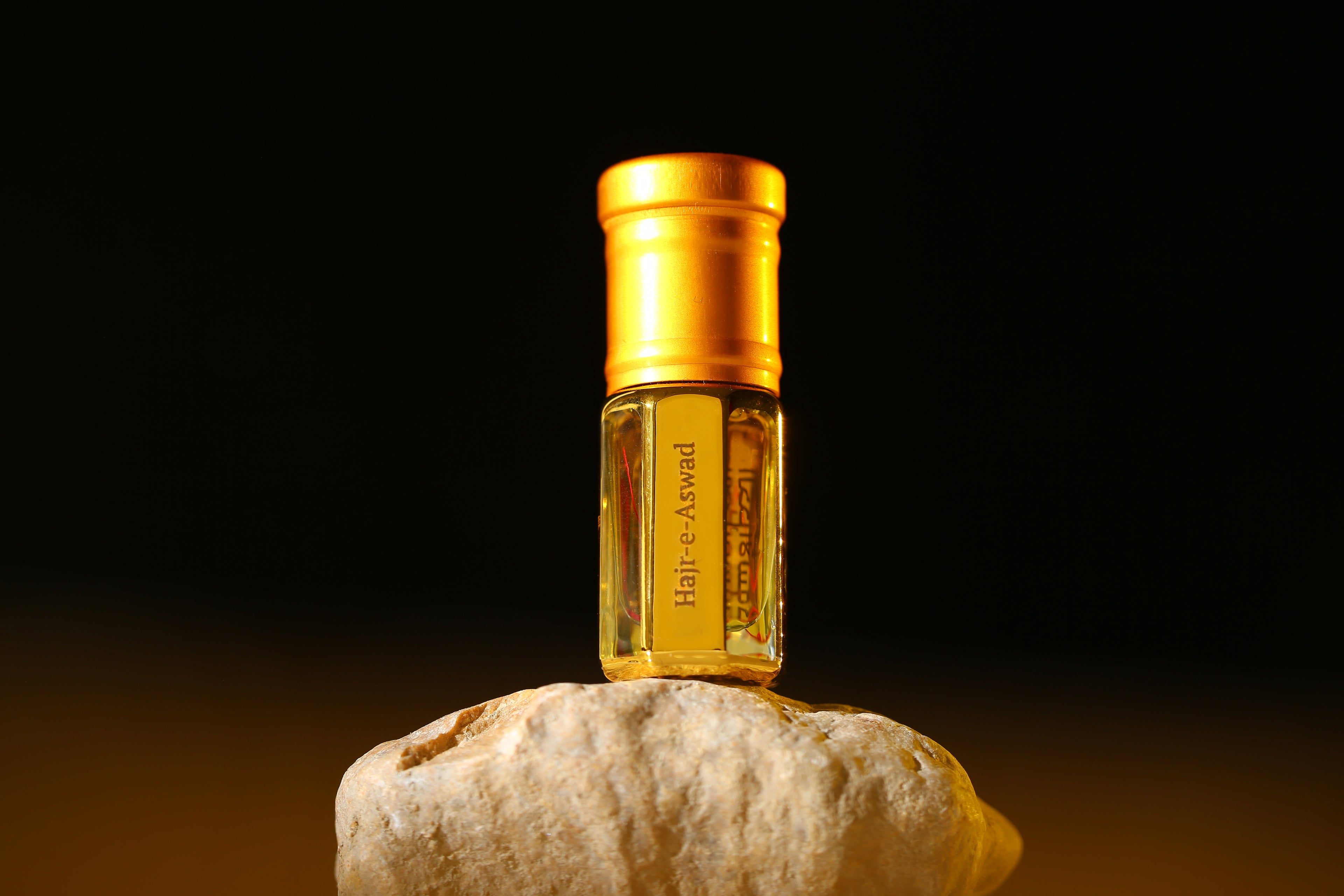 Hajr-e-Aswad Attar by ARK Fragrances in premium gold bottle displayed on stone. Spiritual long-lasting perfume oil inspired by the Holy Black Stone. Best Islamic scent in Pakistan.