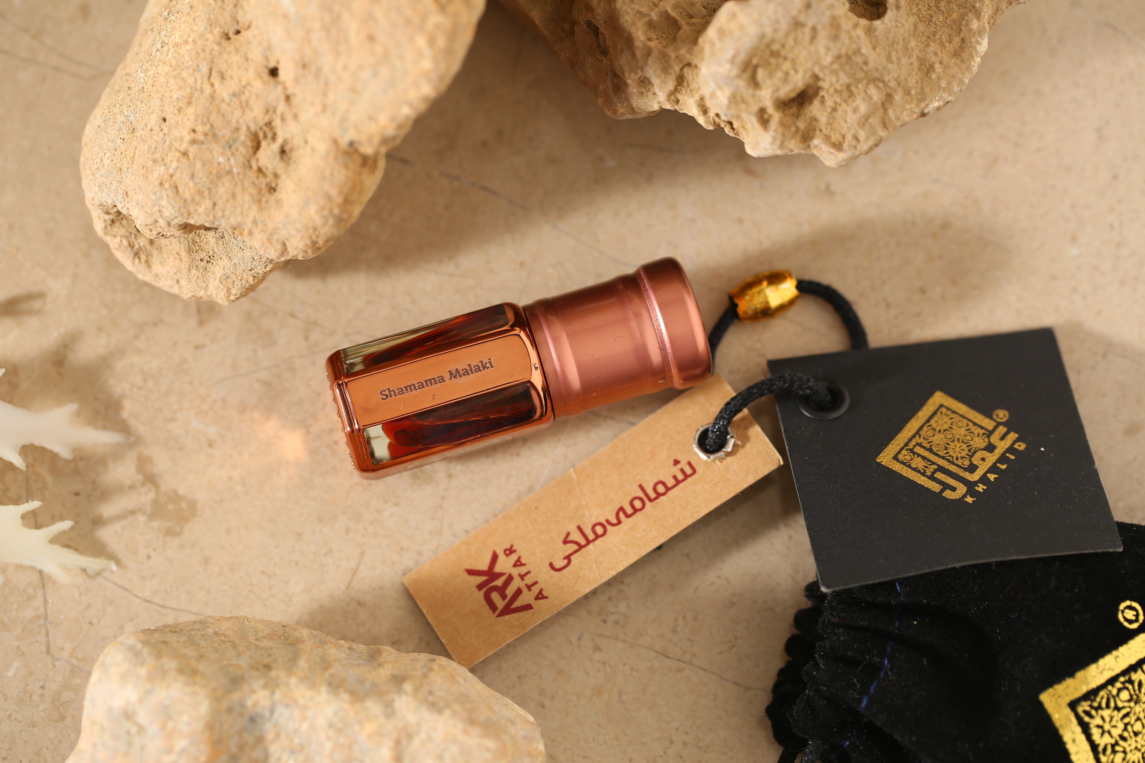 Shamama Maliki Attar by ARK Fragrances 3ml premium concentrated perfume oil with tag and velvet pouch displayed on stone best traditional winter scent online delivery in Lahore Karachi Islamabad Faisalabad and Pakistan