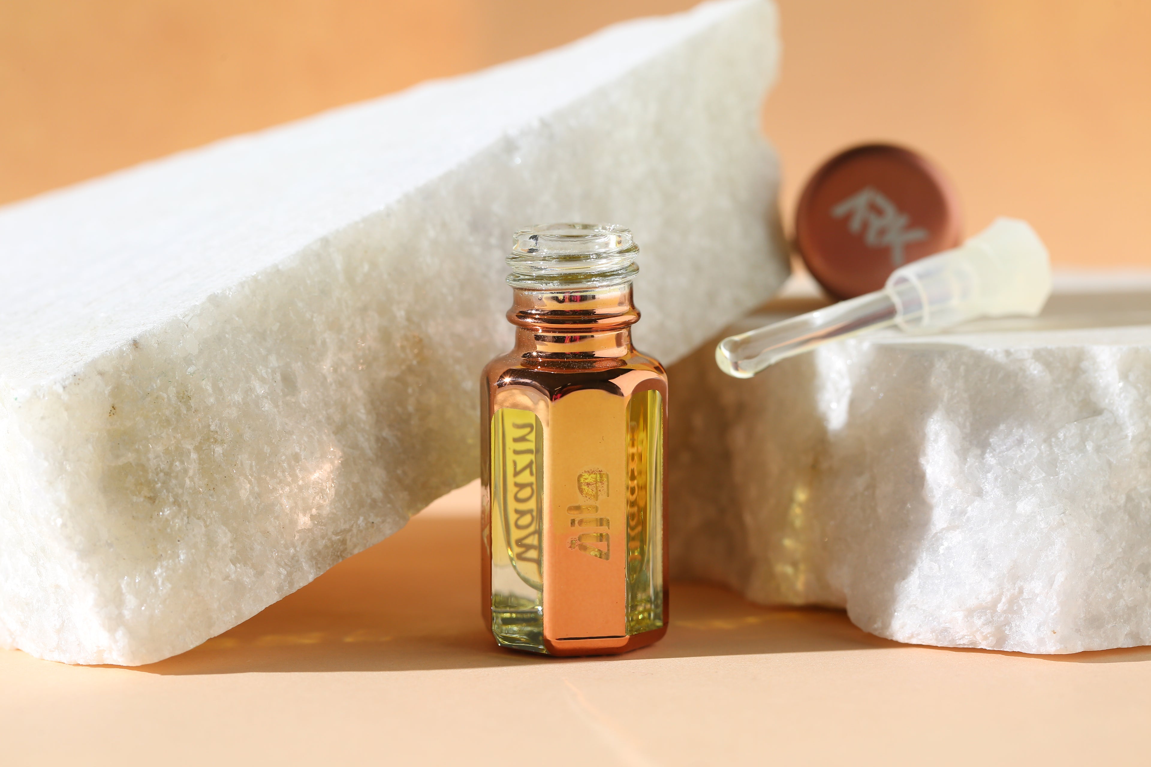 Waazin Attar by ARK Fragrances 3ml premium rose gold bottle displayed on white marble stones with glass stick applicator. We offer long lasting perfume in Karachi, original scent in Lahore, luxury fragrance in Islamabad, best attar shop in Rawalpindi, organic musk in Multan, traditional oud in Peshawar, and fast online delivery in Faisalabad Gujranwala Hyderabad and all over Pakistan