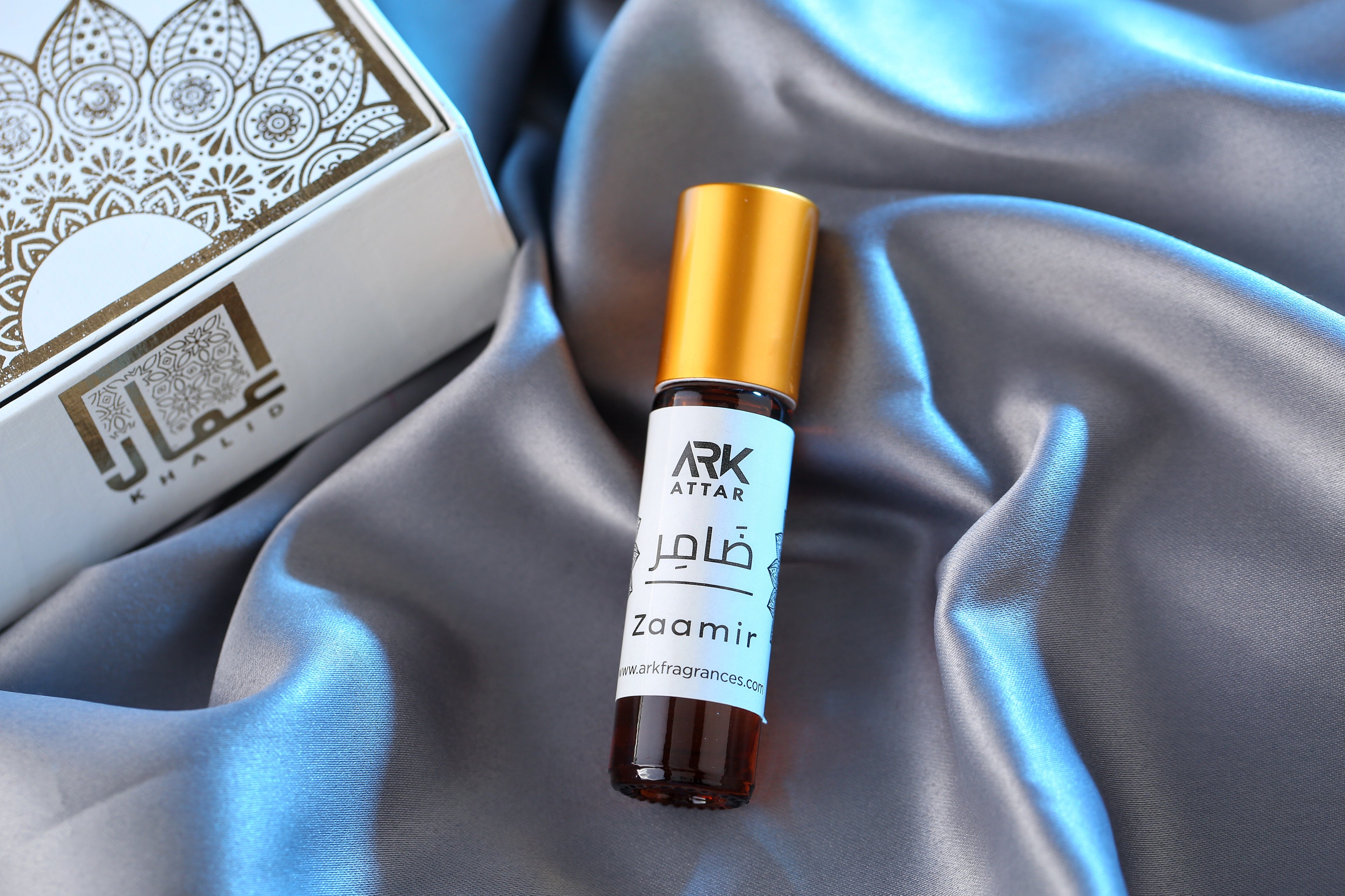 Zaamir Attar by ARK Fragrances 6ml roll on perfume oil displayed on elegant silver satin fabric. This best selling branded perfume features long lasting notes perfect for summer and winter seasons. We offer luxury scent in Karachi, original fragrance in Lahore, premium attar in Islamabad, and fast online delivery in Rawalpindi Multan Peshawar Gujranwala Hyderabad Quetta and all over Pakistan