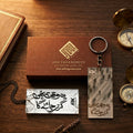 Premium acrylic keychain featuring the Urdu inspirational quote Yeh Waqt Bhi Guzar Jayega, placed next to an ARK Fragrances luxury box and vintage compasses.